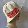 A cream coloured cotton canvas cloche with decorative top stitching on the crown and the brim. The brim can be flipped up and is tapered int he back. There are 3 coral fabric flowers that can be unpinned and worn separately
